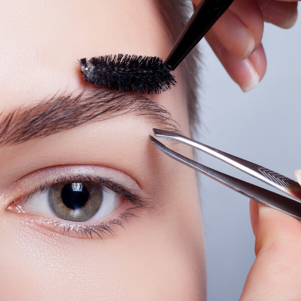Mujer recibiendo perfilado de cejas profesional con pinzas en WAM Center | Clínica Estética. Belleza natural destacada.